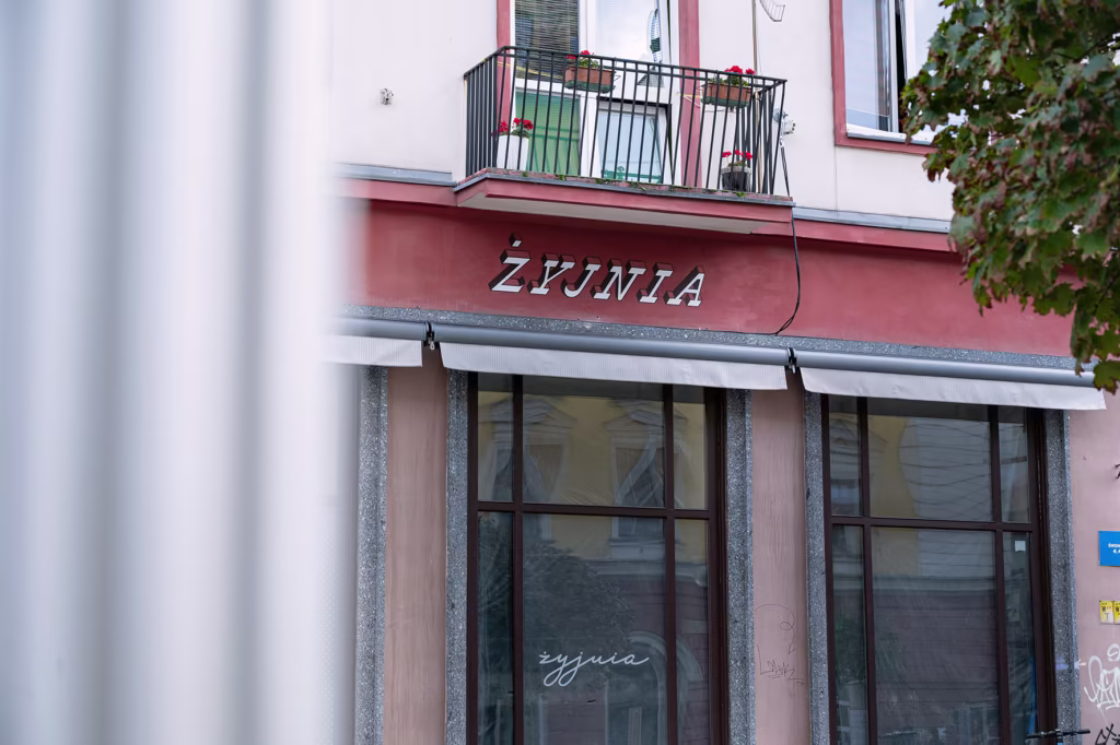 Witryna sklepowa z dużymi oknami i czerwoną fasadą przedstawia napis 