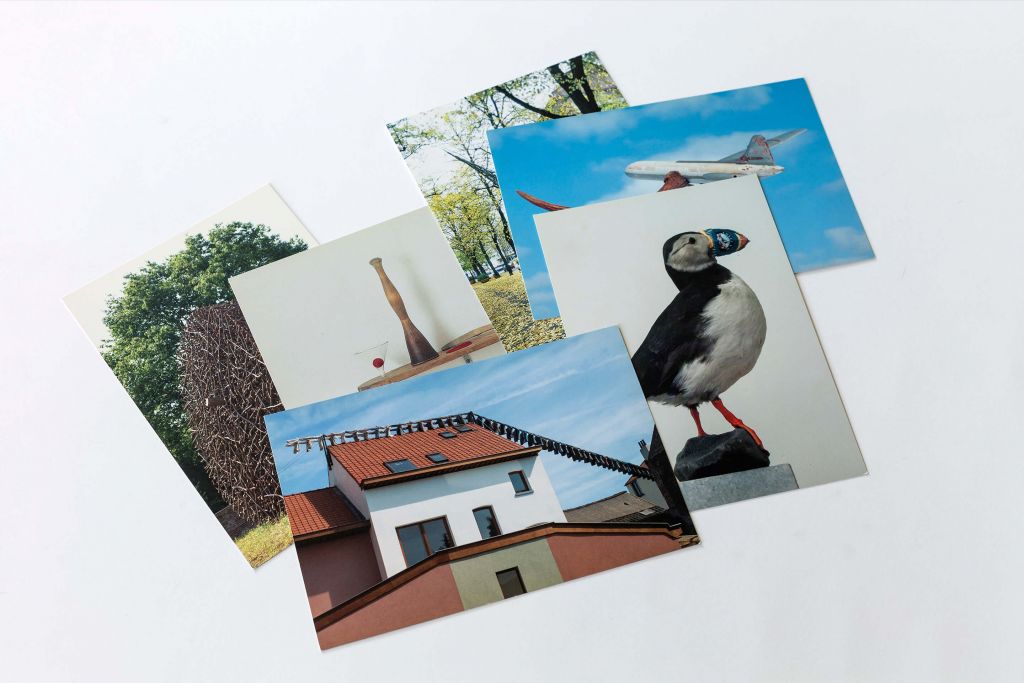Na białym tle rozsypanka z 6 pocztówek – są na nich, budynki, niebo, las i ptak.
