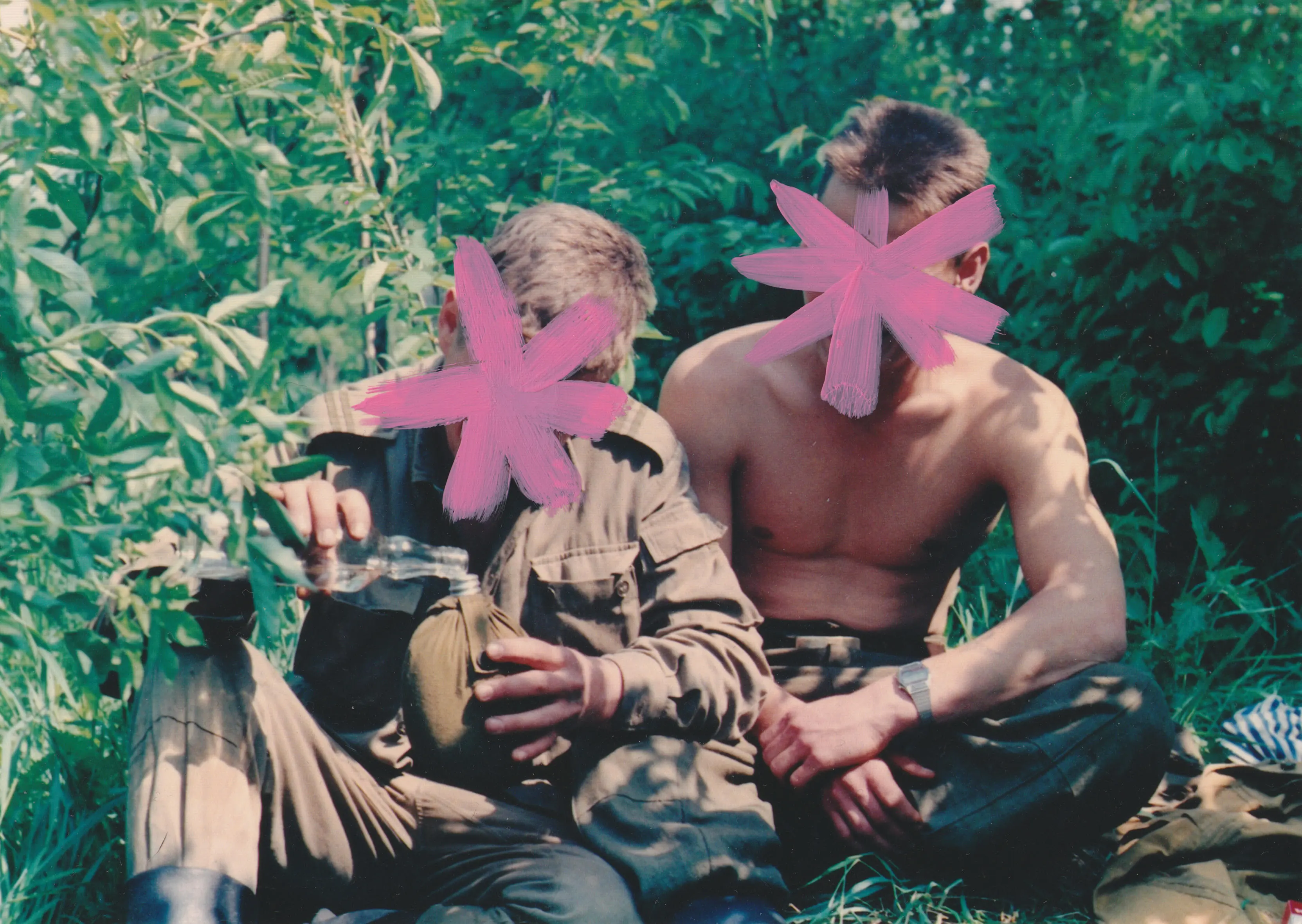 Zdjęcie jest kadrem z filmu "Mon chéri Soviétique" Karola Radziszewskiego. Przedstawia dwóch siedzących wśród zieleni, młodych mężczyzn. Jeden z nich ubrany jest w mundur wojskowy, drugi jest rozebrany do pasa. Mężczyzna w mundurze przelewa przeźroczystą ciecz ze szklanej butelki do bukłaka. Na ich twarzach namalowane są różowe gwiazdy, nie sposób określić ich tożsamości. 