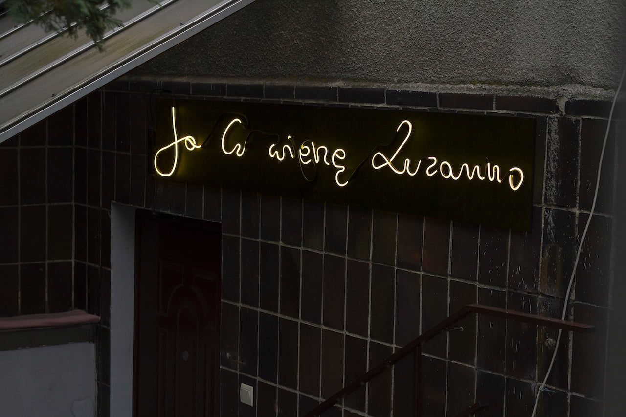 Na ciemnej ścianie budynku neonowy napis Ja Ci wierzę Zuzanno