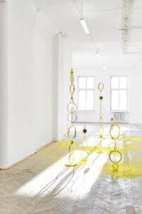 praca rzeźbiarska w postaci żółtych okręgów ułożonych w wieżę w jasnej przestrzeni galerii sztuki