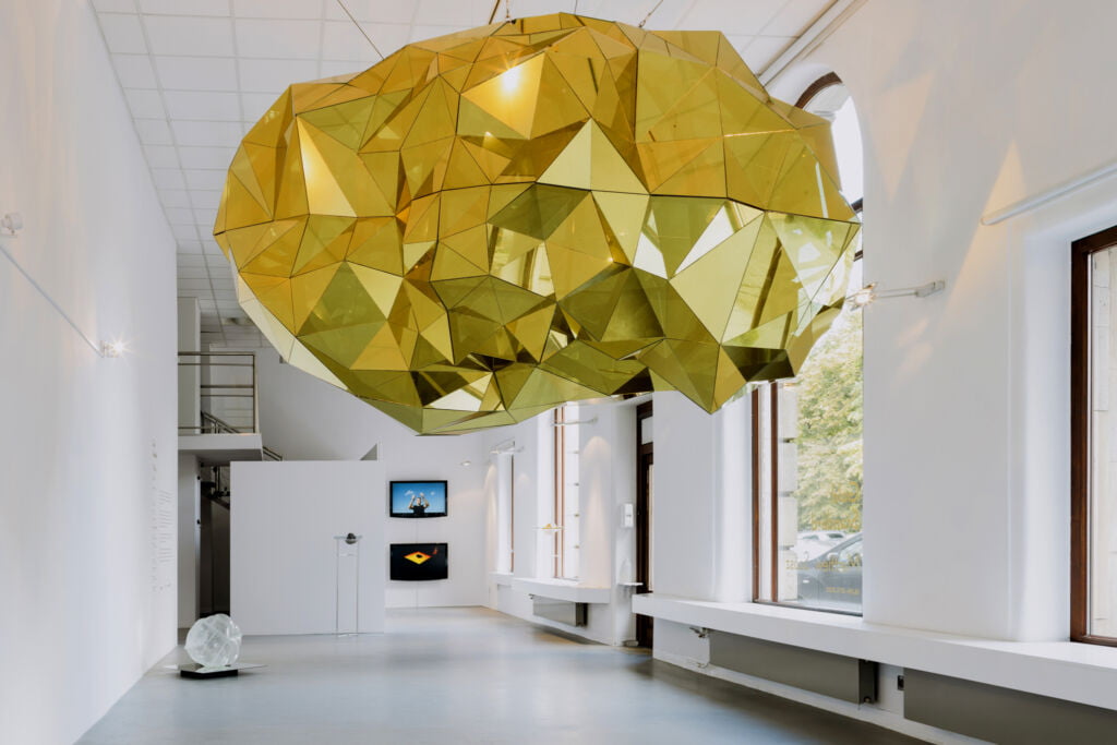 widok wystawy, centralny zawieszony złoty meteoryt, biała przestrzeń galerii