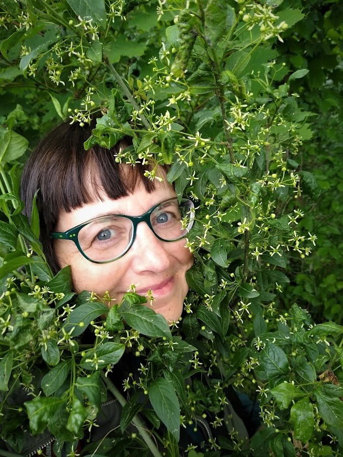 Portret Małgorzaty Piszczek. Na zdjęciu widać głowę otoczoną zielonymi liśćmi krzewu