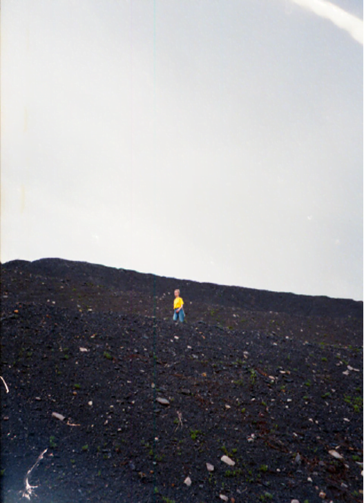 Zdjęcie z czarną ziemią kopalnianej hałdy, na tle której stoi w oddali jedna sylwetka ludzka w żółtym ubraniu