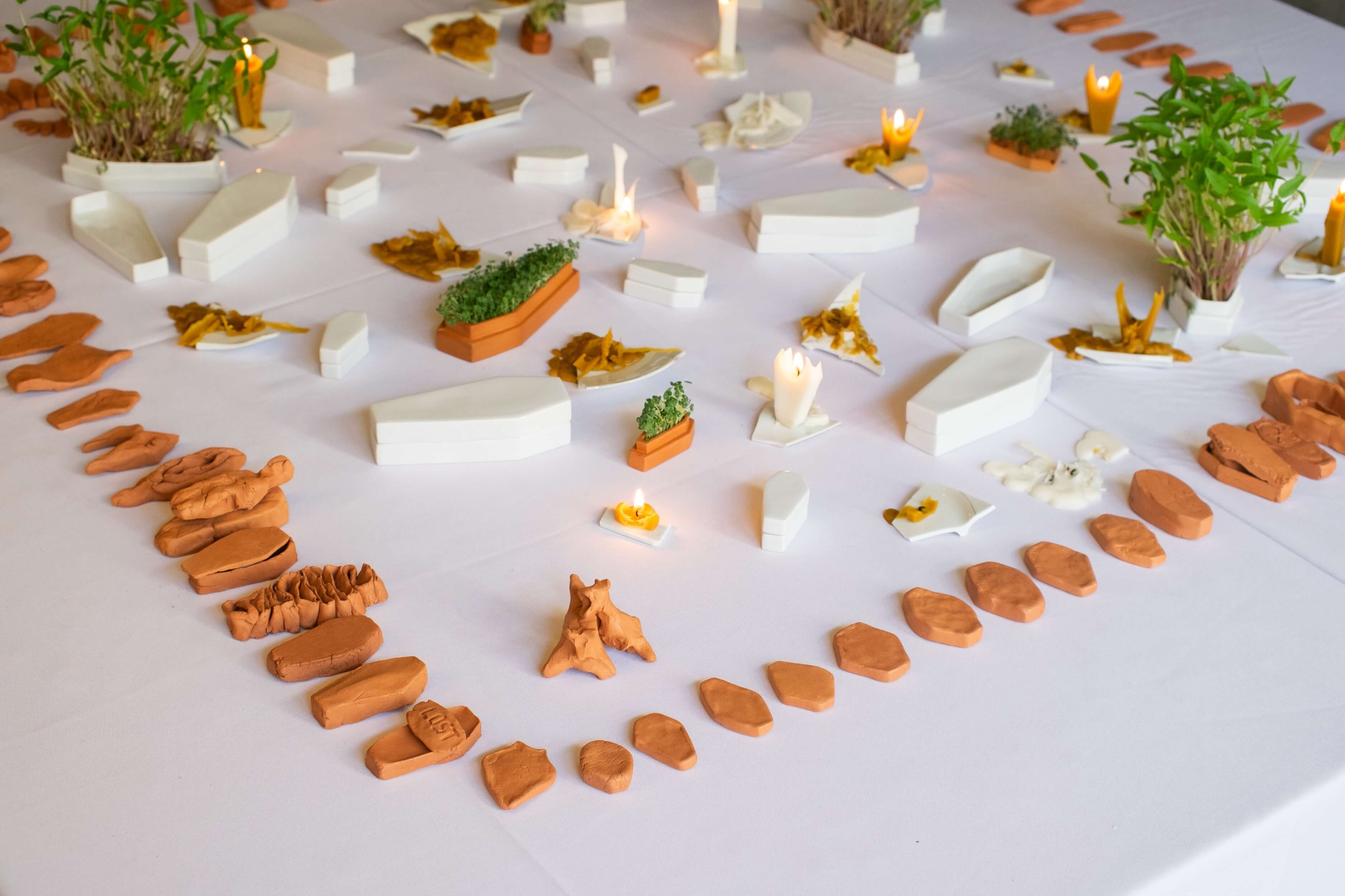 stół z białym obrusem, na którym ułożone są ceramiczne figurki w kształcie trumien, świece i rzeżucha