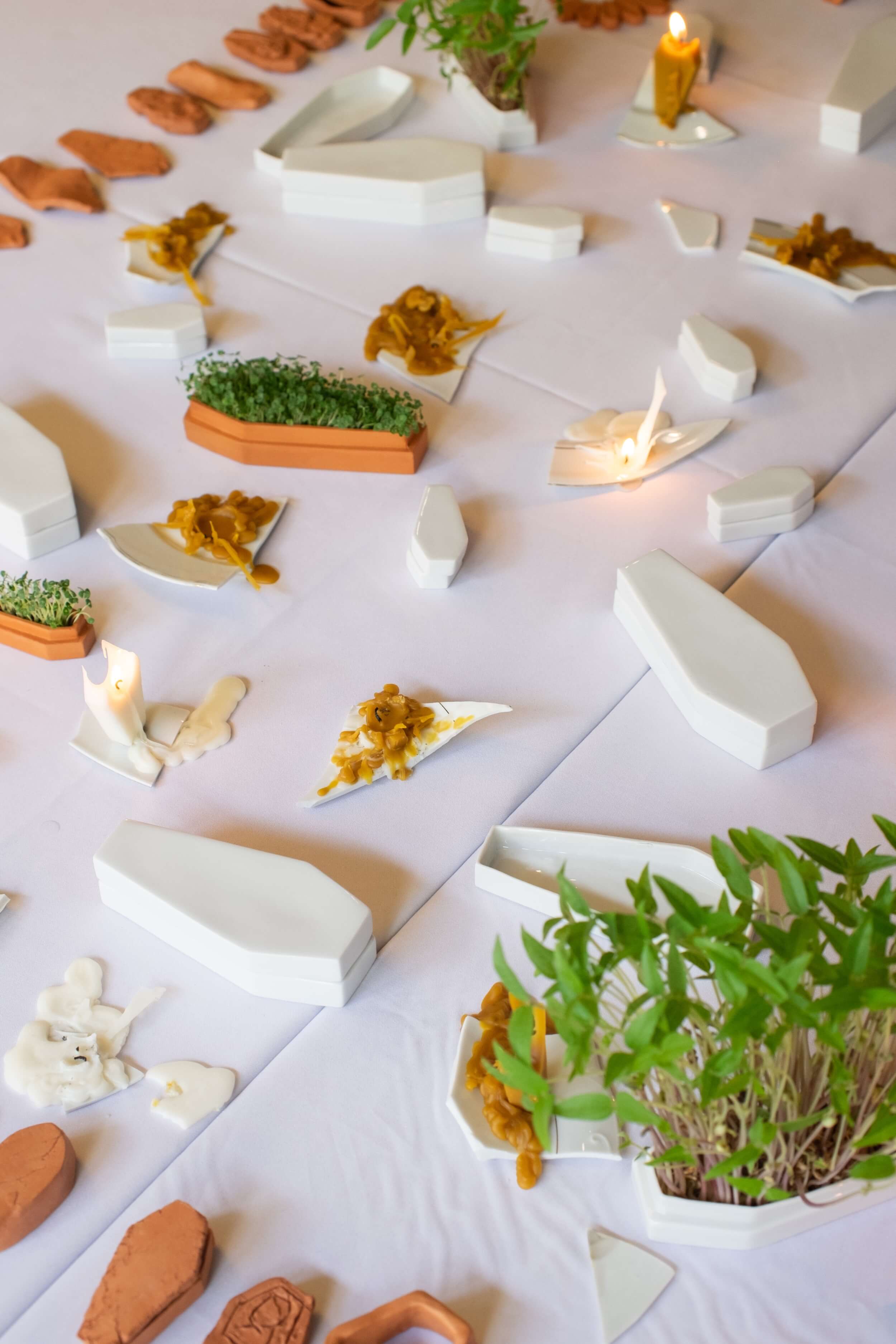 stół z białym obrusem, na którym ułożone są ceramiczne figurki w kształcie trumien, świece i rzeżucha