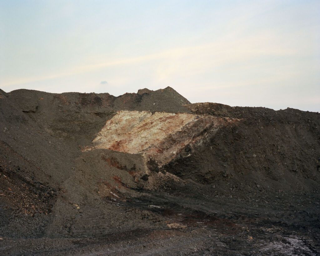 Zdjęcie Michała Łuczaka z cyklu Wydobycie z krajobrazem hałd ciemnych kamieni, prawdopodobnie przy kopalni węgla.