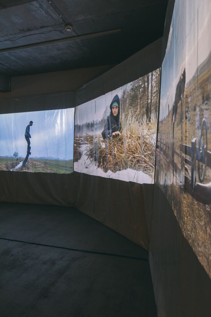Trójkanałowa instalacja video z fragmentami filmu, na którym artysta działa w przestrzeni zaśnieżonego pola.