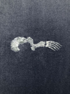 На сірому шматку тканини білою ниткою вишиті кістки плавника тюленя.