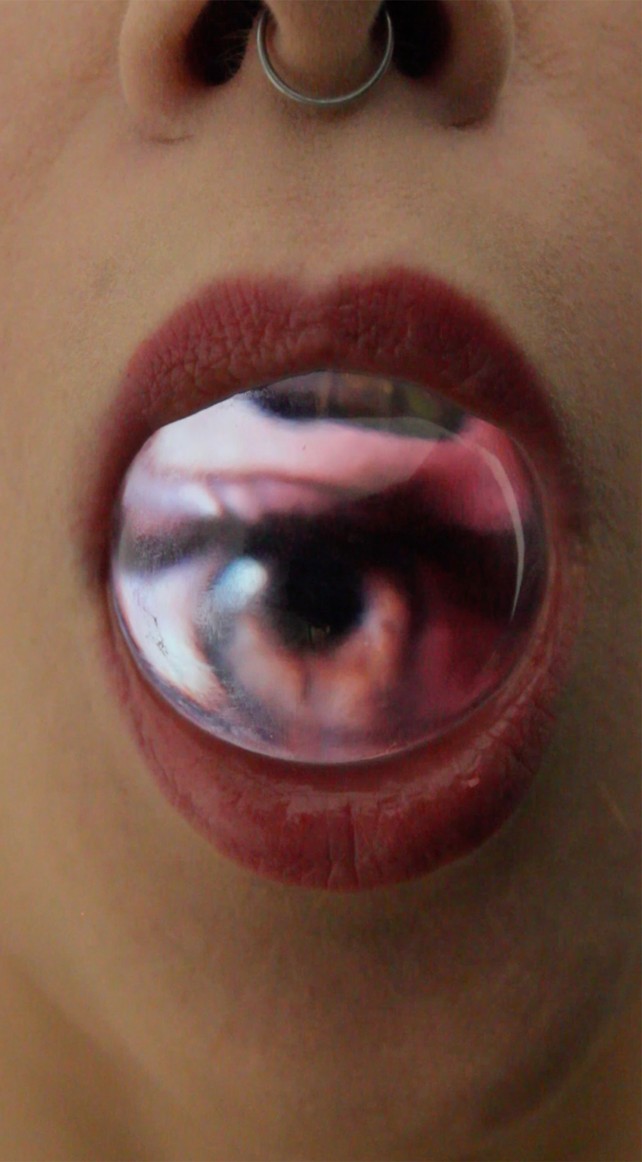 zbliżenie na usta pomalowane szminką, a w nich szklana kula o powierzchni ekranu, na której wyświetla się oko