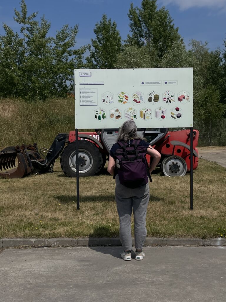 Kobieta z plecakiem patrząca na znak. Tle maszyna rolnicza.