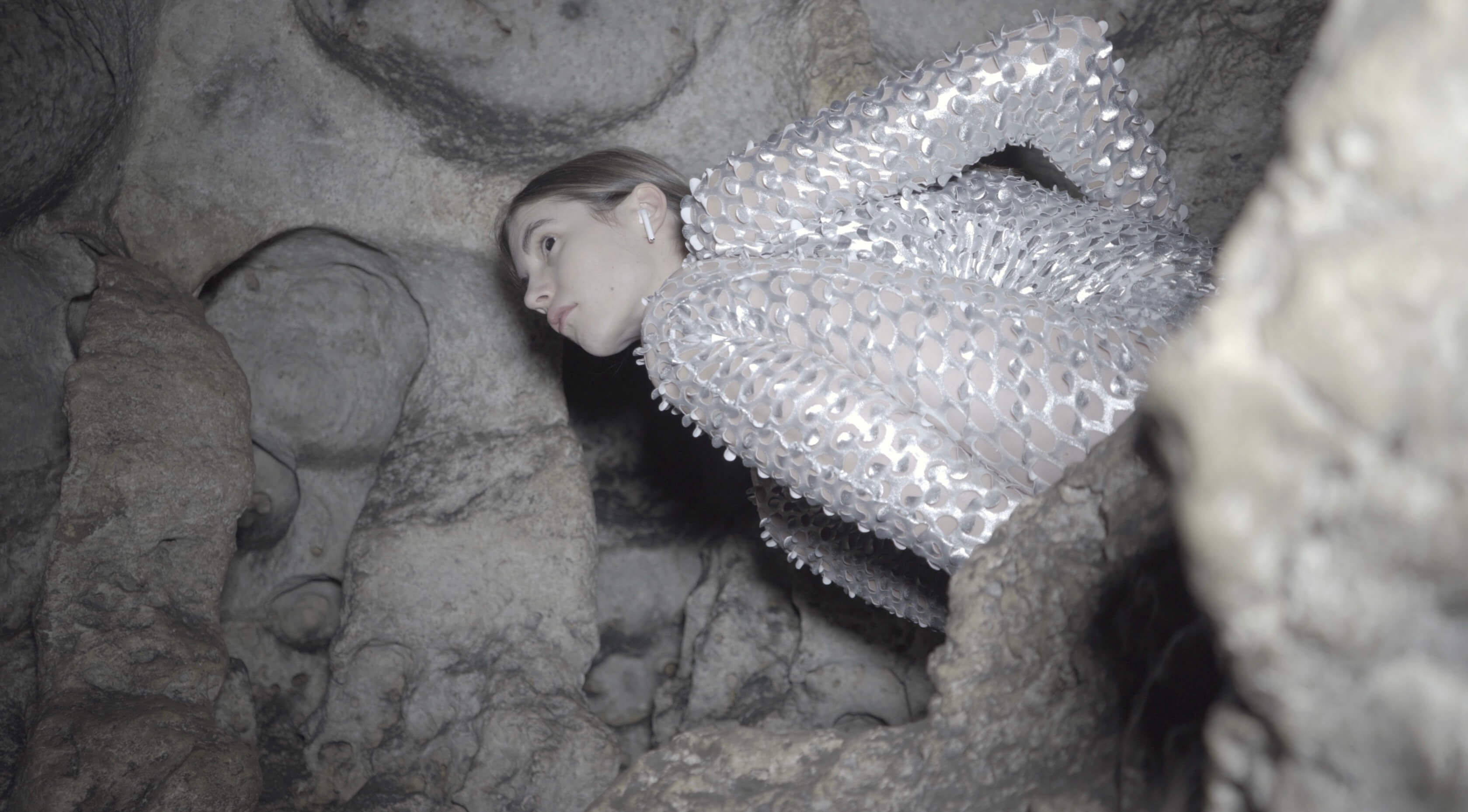 Kobieta w srebrnej sukni stoi w jaskini.