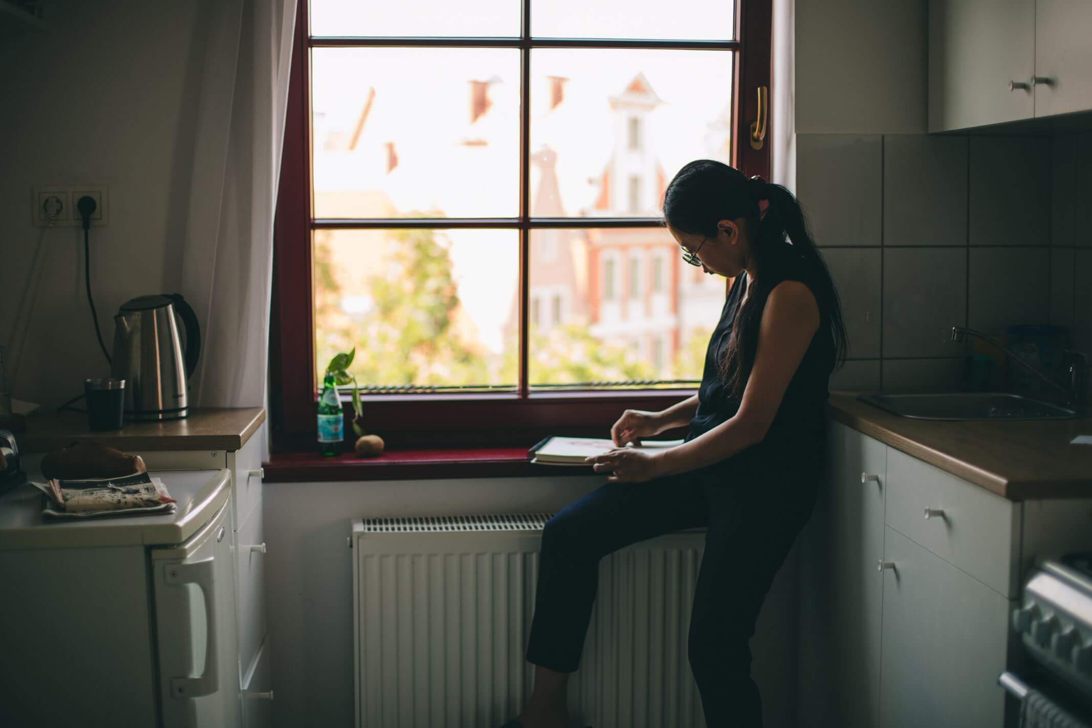 Kobieta siedząca na parapecie okna z tabletem w dłoni.
