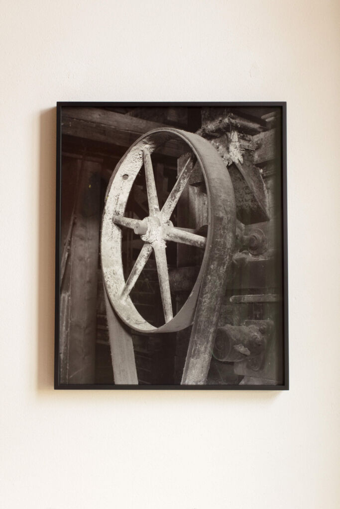 A black and white photograph of a wheel on a wall.