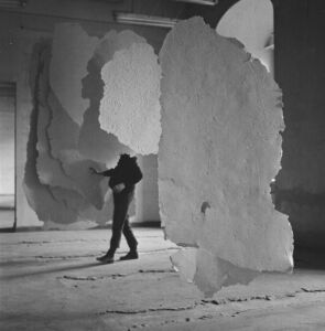 czarno-białe zdjęcie osoby stojącej wśród zwisających betonowych prac ze ściany