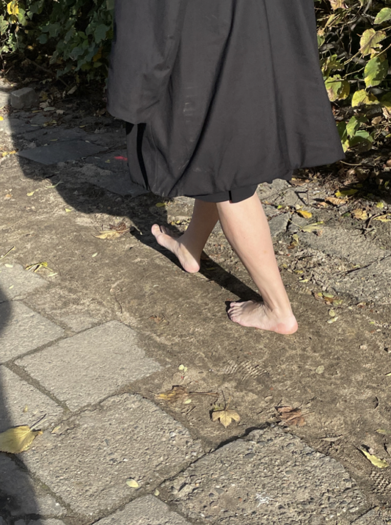 A woman with bare feet walking down a sidewalk.