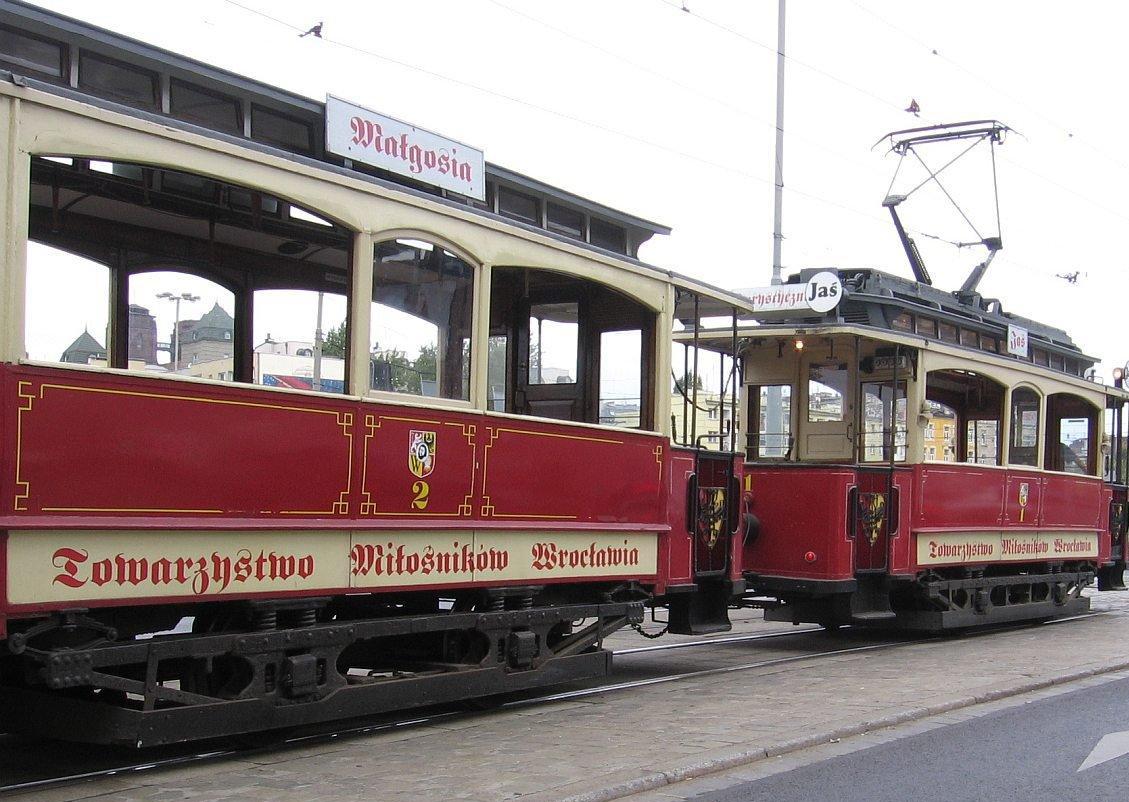 Dwa zabytkowe wagony tramwajowe, w kolorach czerwonymi kremowym, stoją na torach tramwajowych