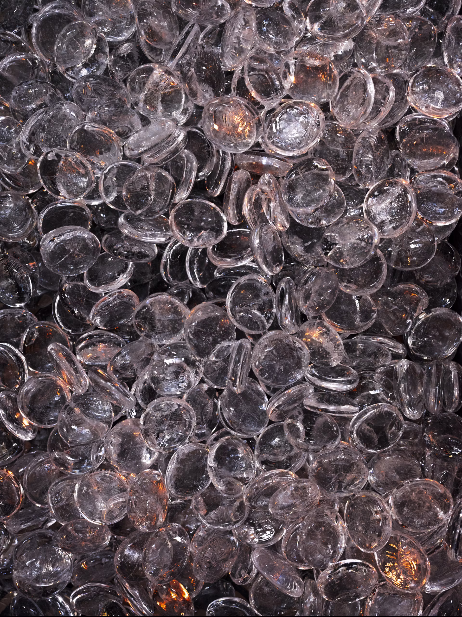 Widok z bliska wielu przezroczystych, okrągłych szklanych lub plastikowych dysków ułożonych jeden na drugim i zachodzących na siebie z pomarańczowymi refleksami świetlnymi.