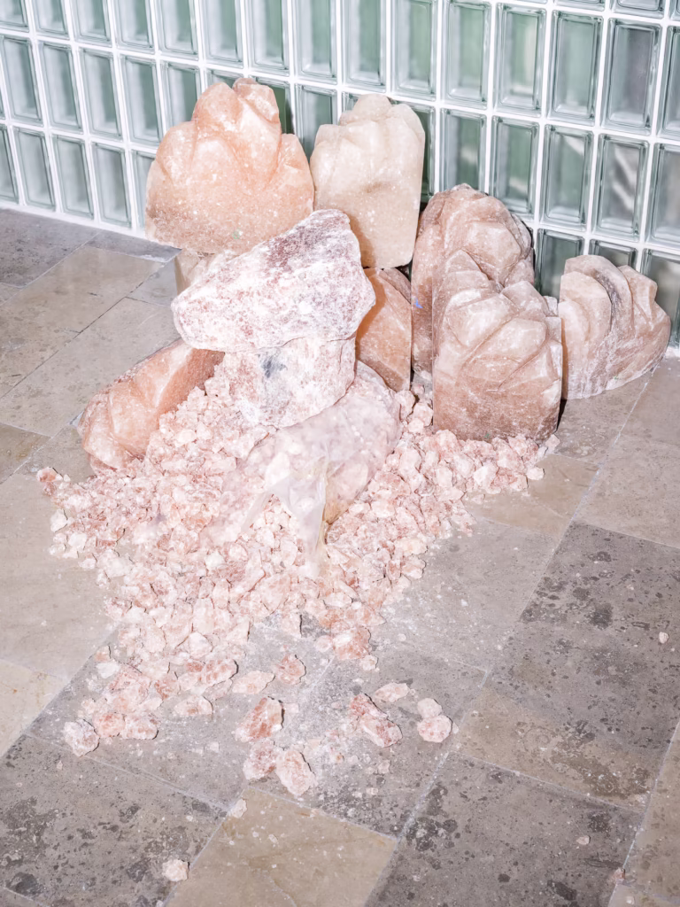 Stos dużych i małych różowych skał solnych leży na wyłożonej kafelkami podłodze przed szklaną ścianą.
