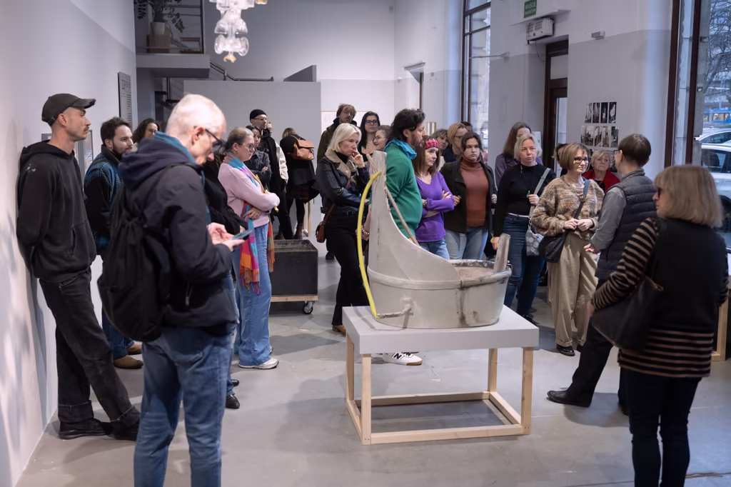 Grupa ludzi gromadzi się wokół rzeźby umieszczonej na cokole w galerii sztuki współczesnej.