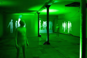 W oświetlonym na zielono pomieszczeniu BWA Wrocław stoi kilka ludzkich postaci w kombinezonach, a na ścianach wyświetlane są sylwetki podobnych postaci.