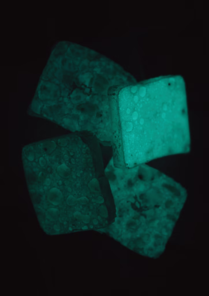 Cztery kwadratowe obiekty o nakrapianej teksturze świecą zielonkawo-niebieskim światłem w ciemnym otoczeniu.