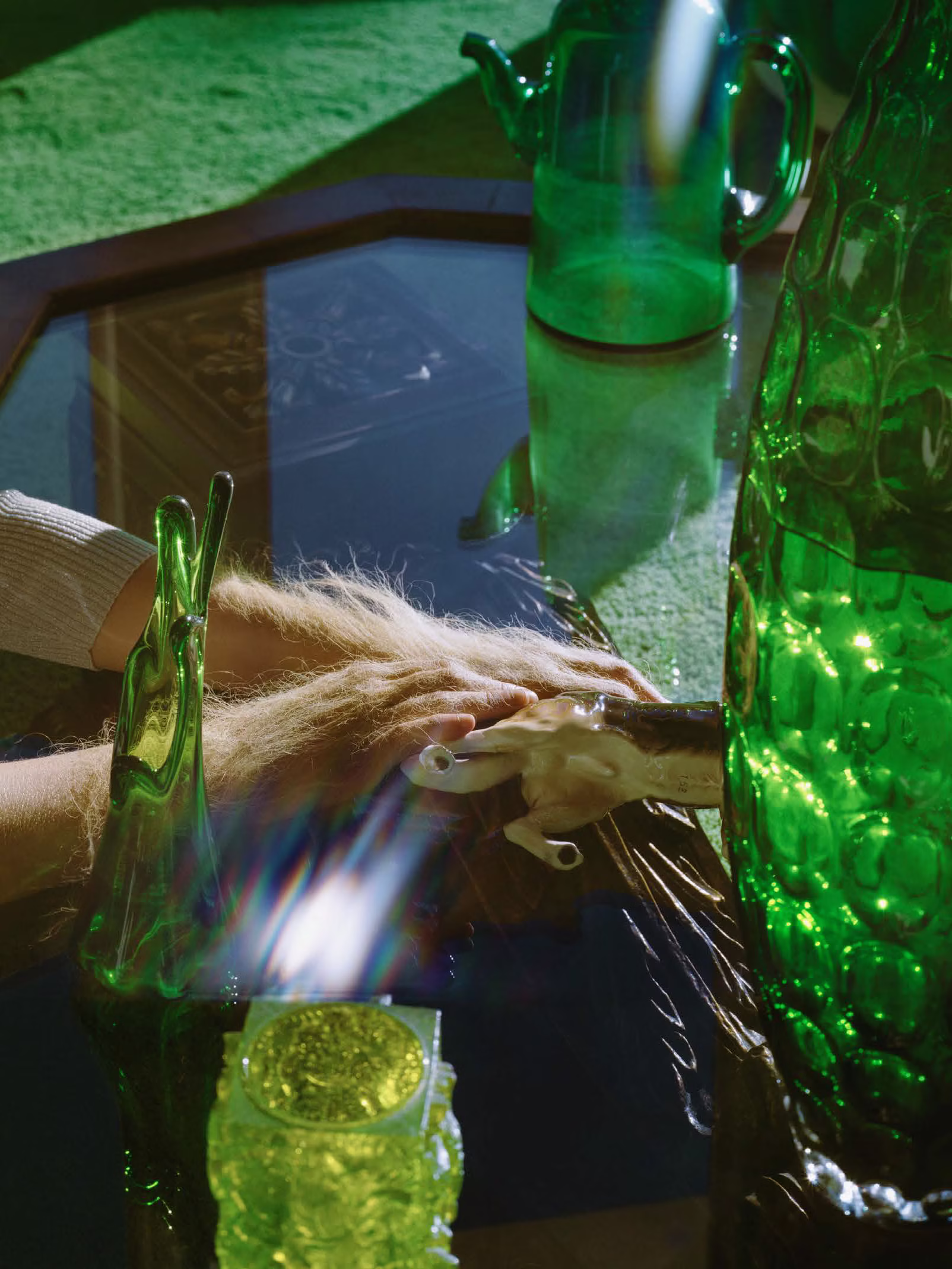 Ludzka dłoń i zwierzęca łapa dotykają odblaskowej powierzchni, otoczonej zielonymi szklanymi obiektami i oświetlonej światłem słonecznym.