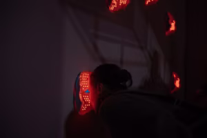 Osoba wchodzi w interakcję z czerwoną podświetlaną maską zamontowaną na ścianie, z kilkoma podobnymi świecącymi maskami widocznymi w tle.